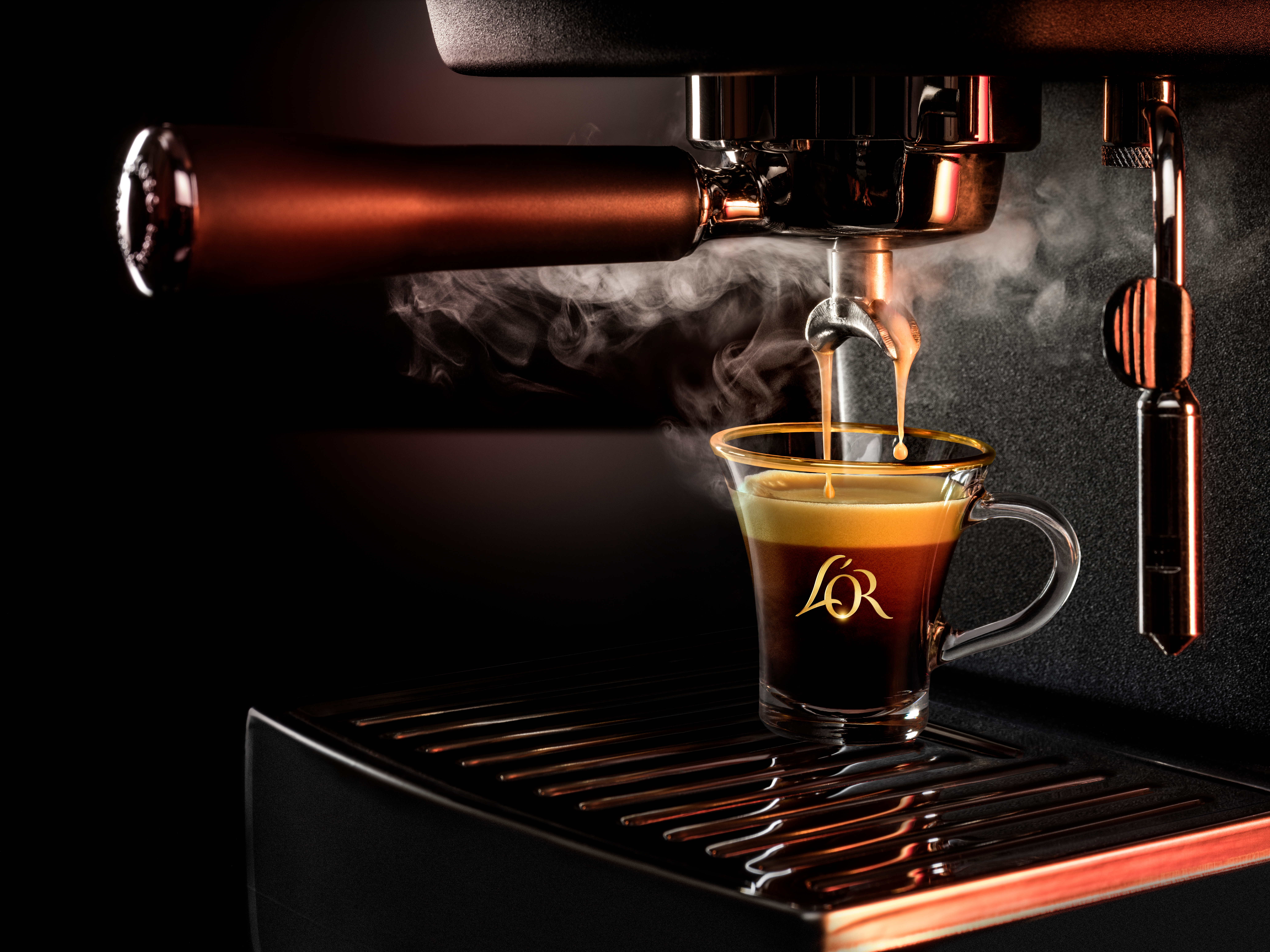 Nahaufnahme einer Espressomaschine, die Espresso in eine Glastasse mit "L'OR"-Logo gießt, mit aufsteigendem Dampf.